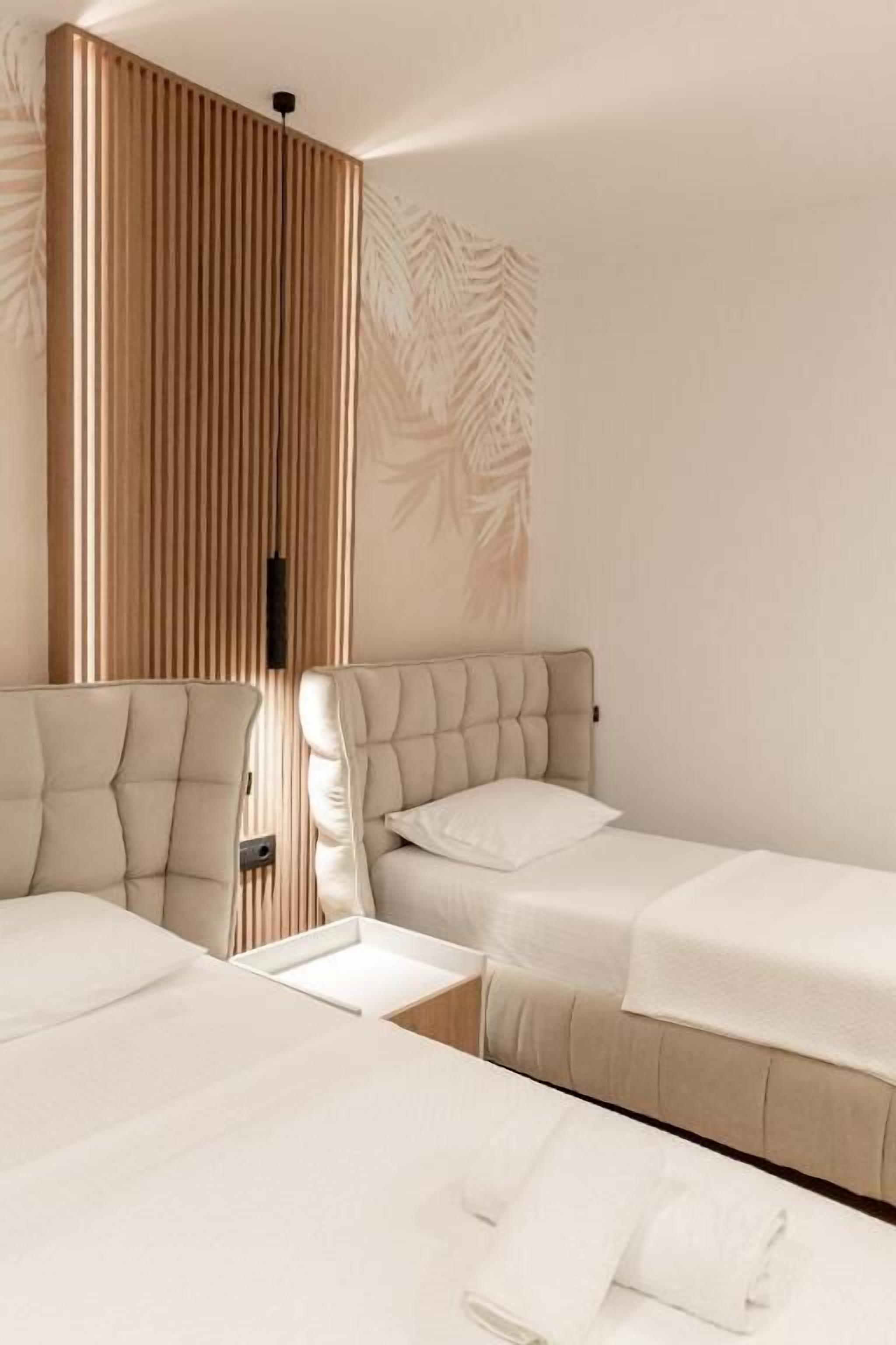 A hotel room with two beds, a wooden panel wall, and a leaf-patterned wall.