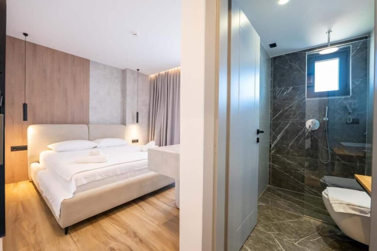 A modern bedroom with a large bed, a wooden accent wall, and a separate bathroom with a glass shower enclosure.