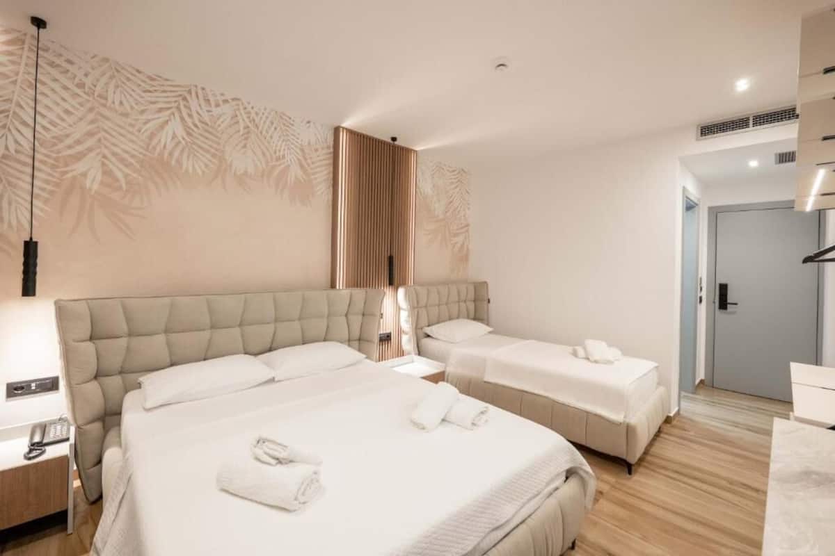 A hotel room with a large bed, two smaller beds, a desk, and a wardrobe.