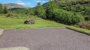 A gravel parking area with a stone wall, surrounded by green grass and trees. - THE SKATING ROCK, pet friendly in Kenmare, County Kerry (Bonane)