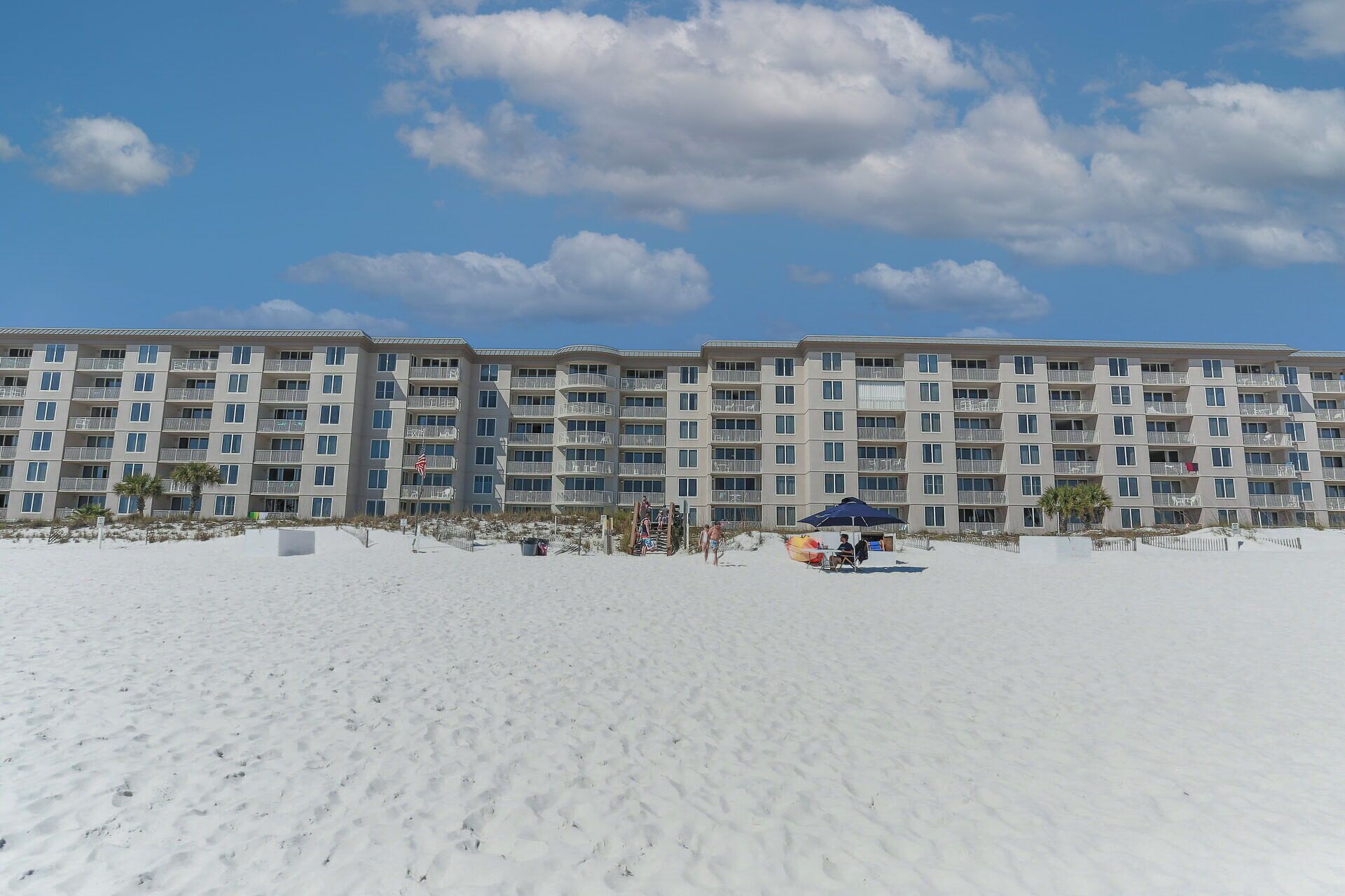 Un hôtel situé en bord de mer, doté de nombreux balcons, d’une plage de sable fin et offrant une vue sur un ciel dégagé.