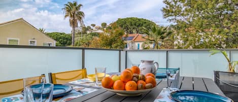 Un área de comedor al aire libre con una mesa dispuesta para dos, que incluye un frutero y una jarra.