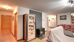 A cozy living room with a wooden cabinet, a black wood-burning stove, and a covered sofa. - La Perle de Xonrupt - Appt vue montagne (Xonrupt-Longemer)