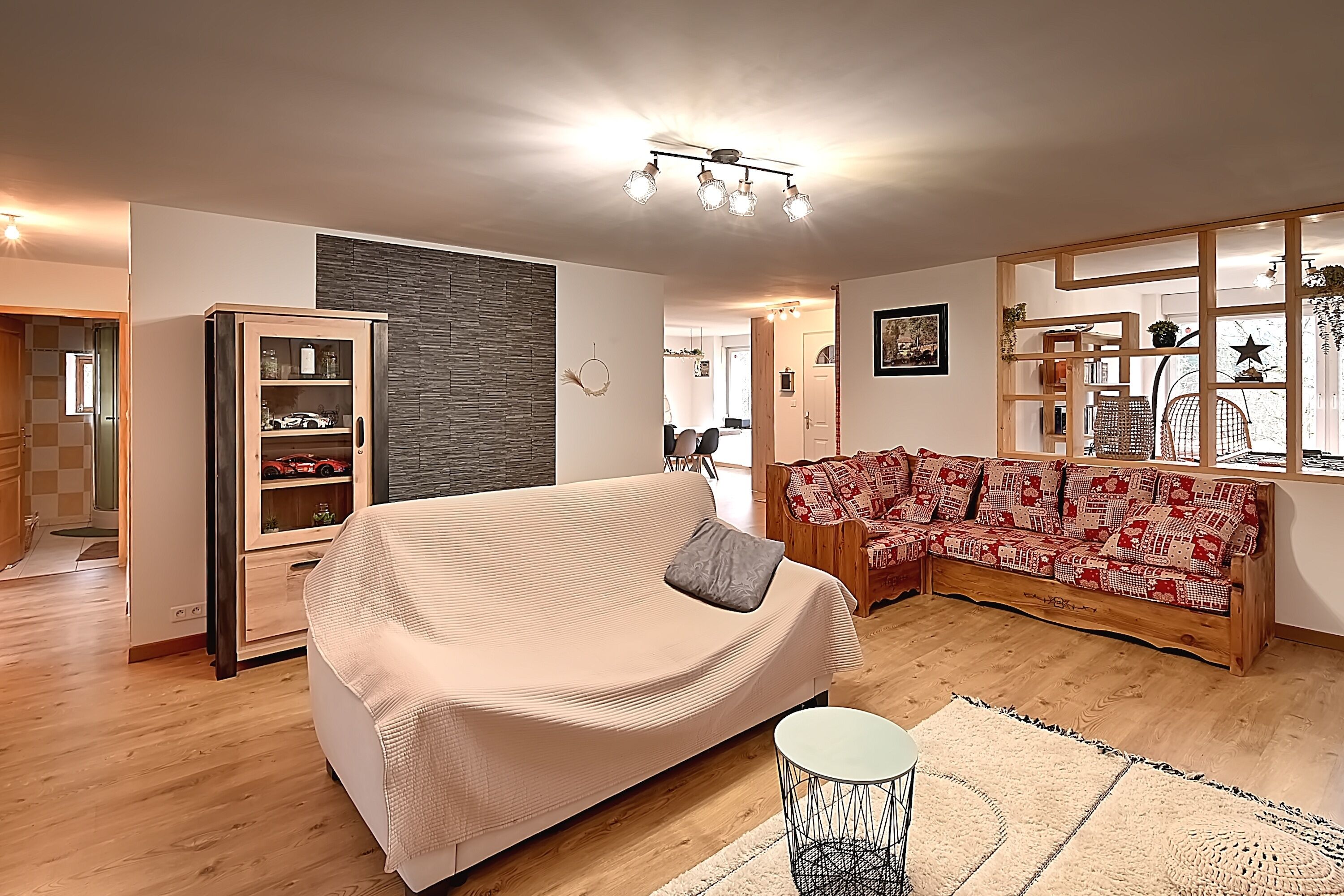 A modern living room with a beige sofa, a wooden cabinet with glass doors, and a patterned sofa.