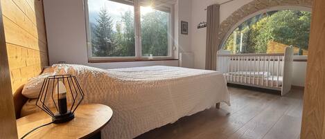 A bedroom with a large window, a crib, and a wooden floor.