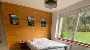 A bedroom with a wooden wall, a bed, a crib, and a window with a view of greenery. - La Perle de Xonrupt - Appt vue montagne (Xonrupt-Longemer)