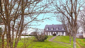 Ein großes, zweistöckiges Haus mit einem steilen Dach, umgeben von einem gepflegten Rasen und Bäumen.