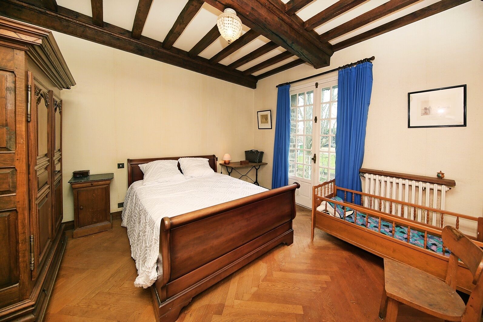 Ein traditionell eingerichtetes Schlafzimmer mit einem hölzernen Bett, einem kleinen Nachttisch, einem Heizkörper und einer Holzbank mit Polsterung.