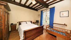Ein traditionell eingerichtetes Schlafzimmer mit einem hölzernen Bett, einem kleinen Nachttisch, einem Heizkörper und einer Holzbank mit Polsterung.