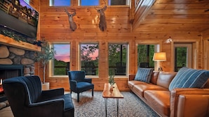 A cozy cabin interior with a fireplace, leather furniture, and a scenic view through large windows.