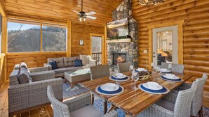 A log cabin interior with a fireplace, dining table set for six, and a cozy seating area.