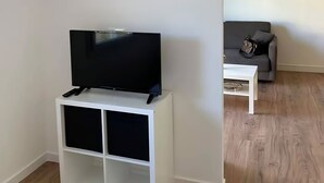 A room with a white TV stand, a grey sofa, and a white coffee table. - Appartement à 5 Minutes des Plages - 42m2 - Jardin Privatif et Parking Privé (Carqueiranne)