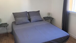 A bedroom with a bed, two bedside tables, a window with curtains, and a wooden floor. - Appartement à 5 Minutes des Plages - 42m2 - Jardin Privatif et Parking Privé (Carqueiranne)