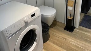 A compact bathroom with a white washing machine, a toilet, and a small mirror. - Appartement à 5 Minutes des Plages - 42m2 - Jardin Privatif et Parking Privé (Carqueiranne)