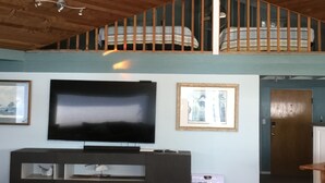 A spacious living room with a large flat-screen TV, wooden ceiling, and a staircase leading to an upper level. - Stunning beach house with pool and hot tub. Pet friendly! Great for families!  (Bellingham)