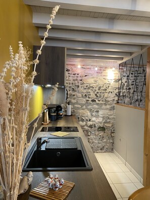 Kitchen features a black sink, contemporary faucet, and wooden countertop, with pendant lights and a stone wall.