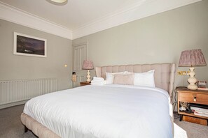 A neatly made bed with a white comforter and pillows, a wooden nightstand with a lamp, and a framed picture on the wall. - Charming 3BD Oasis 3 Min Walk From Beach Front! (Dublin)