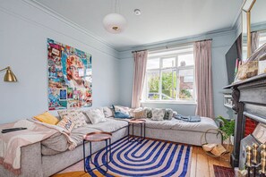 A cozy living room with a sectional sofa, a blue and white striped rug, a fireplace, and a large poster on the wall. - Charming 3BD Oasis 3 Min Walk From Beach Front! (Dublin)