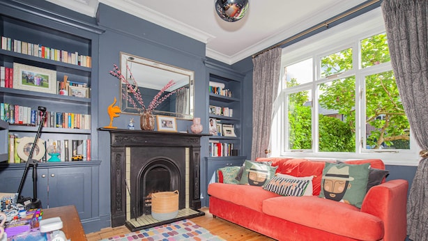 A cozy living room with a fireplace, bookshelves, a red sofa, and a large window with a view of greenery. - Charming 3BD Oasis 3 Min Walk From Beach Front! (Dublin)