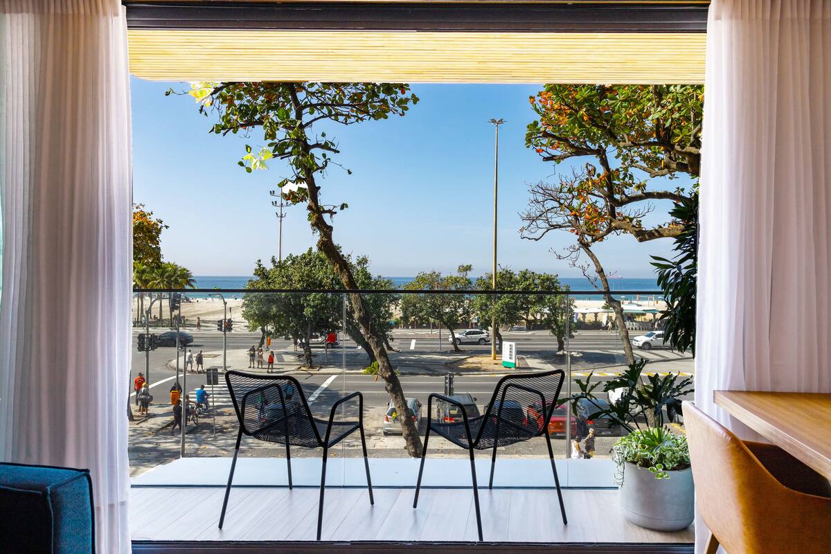 Ein Balkon mit zwei Stühlen, einem Topfpflanzen und Blick auf eine Straße und den Strand.