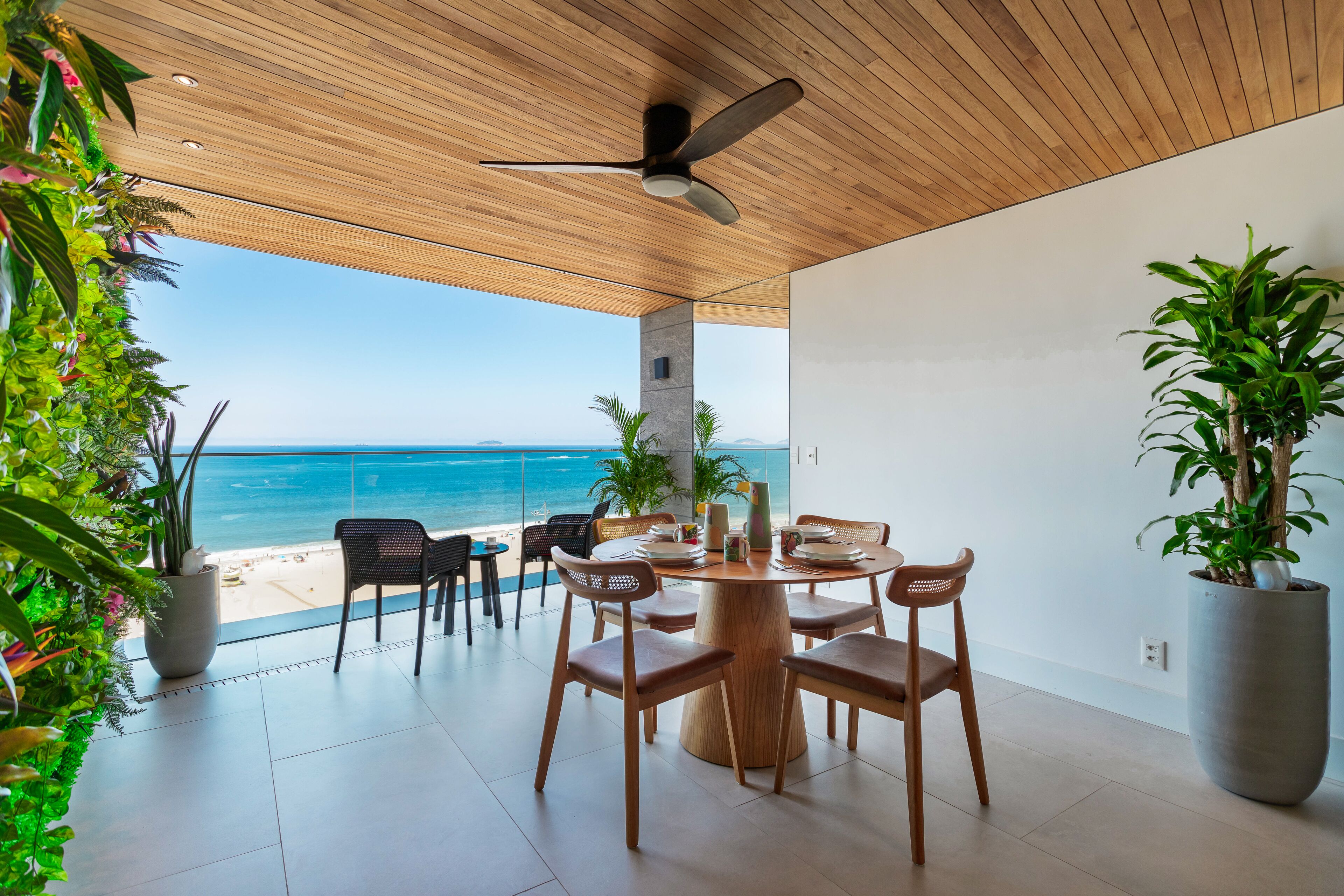 A dining area with a view of the ocean, wooden ceiling, and potted plants.