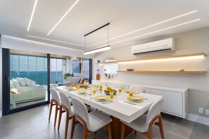 A modern dining area with a long table set for four, a sofa by a large window, and an air conditioning unit on the wall. - Unhotel (Rio de Janeiro)