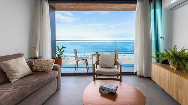A modern living room with a view of the beach, a sofa, a chair, and a coffee table. - Unhotel (Rio de Janeiro)