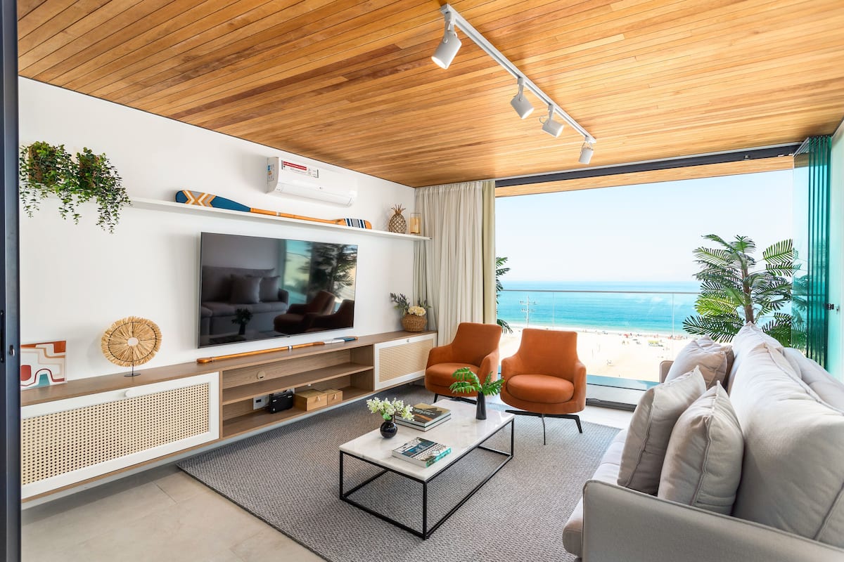 Ein modernes Wohnzimmer mit großem Fernseher, bequemen Sitzmöglichkeiten und Blick auf den Strand.