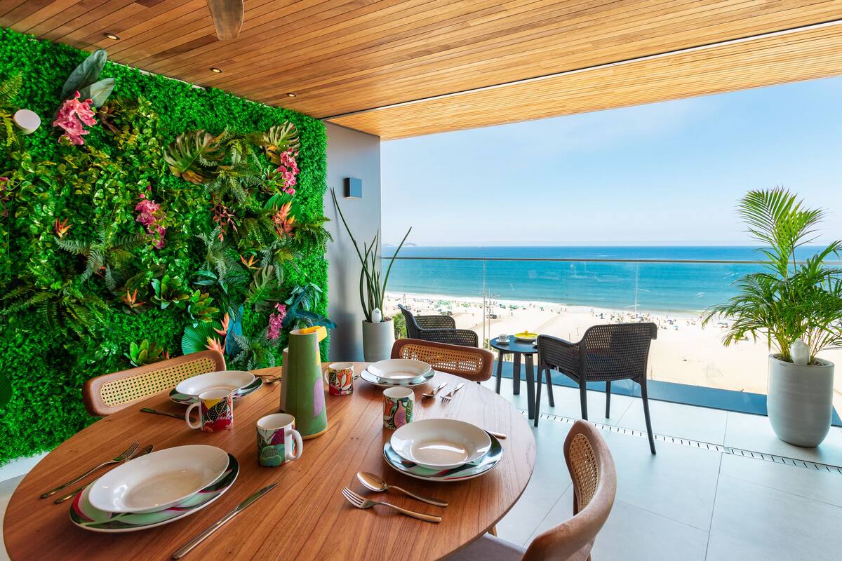 Ein Essbereich mit Blick auf den Strand, eine grüne Wand mit Pflanzen und eine Holzbalkendecke.