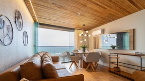 A modern living room with a wooden ceiling, a large window overlooking the ocean, a dining area with a table and chairs, and a sofa with a basket. - Unhotel (Rio de Janeiro)
