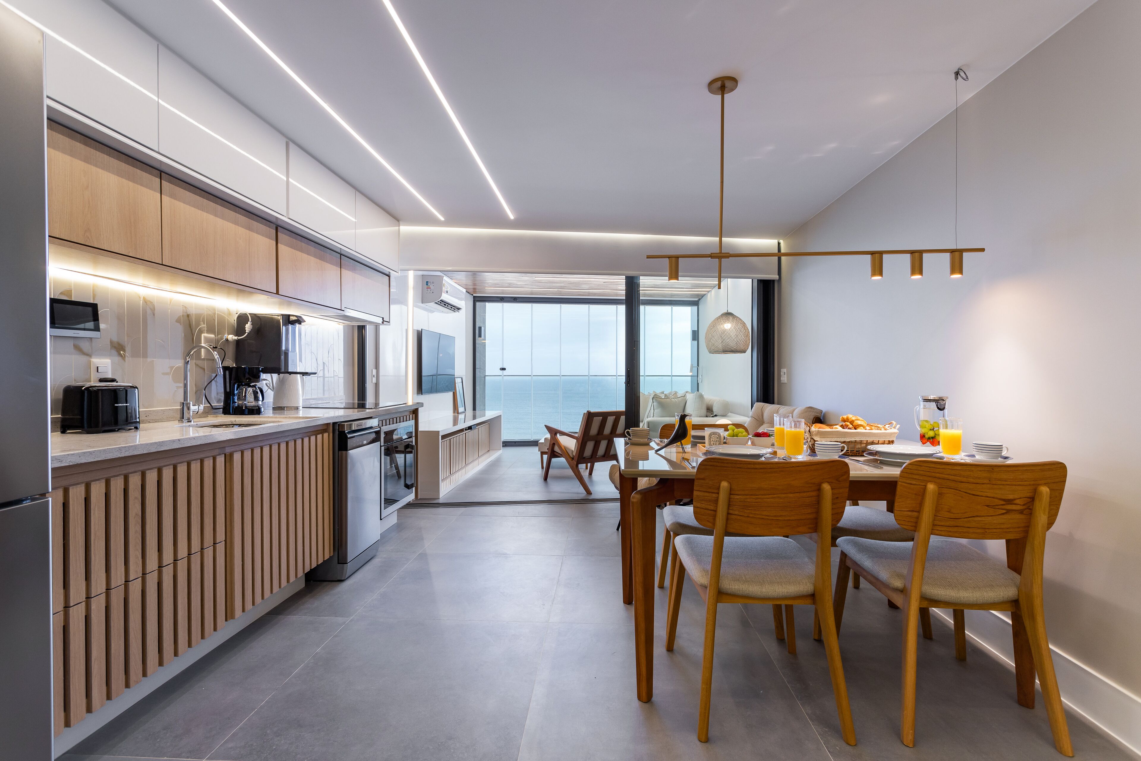 Une cuisine moderne avec des meubles en bois, un coin repas avec des chaises en bois et une vue sur l’extérieur.