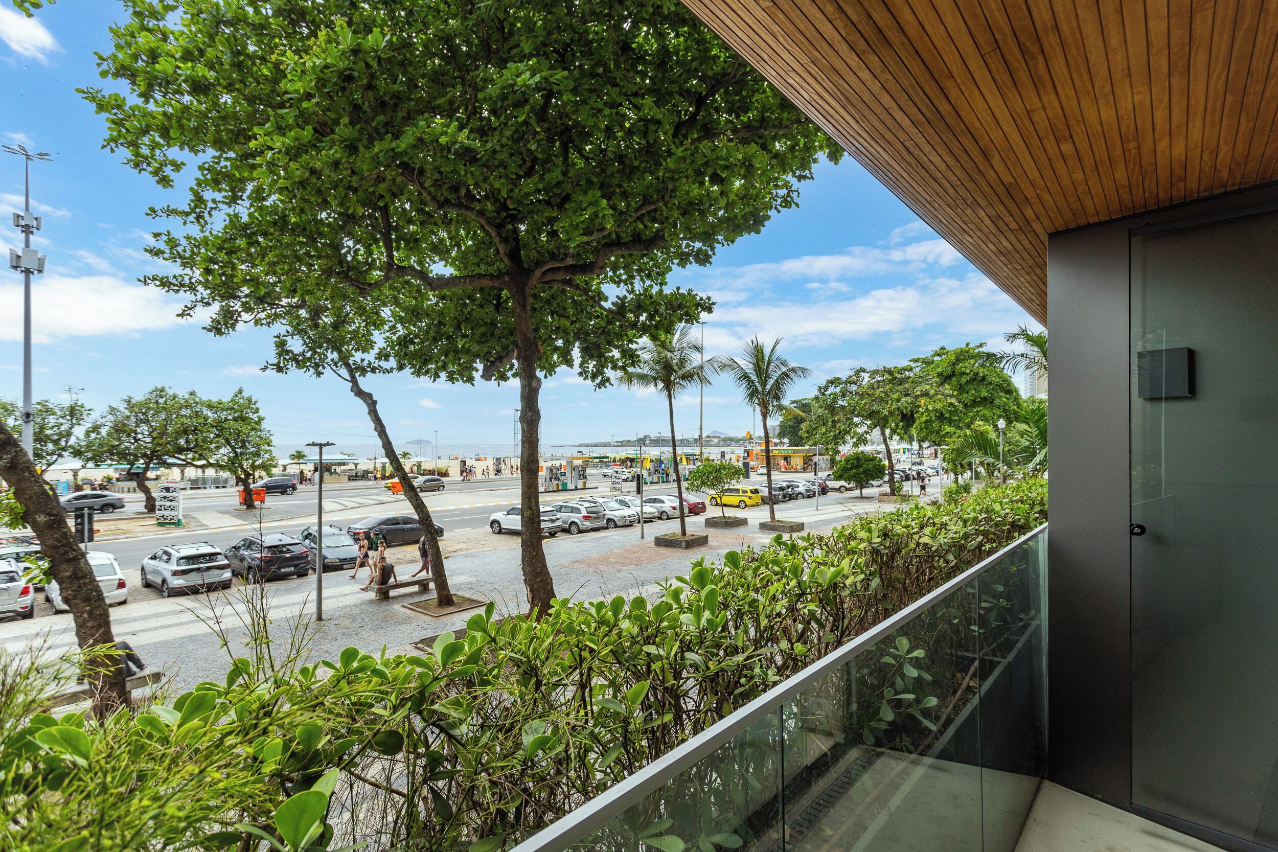 A modern building with a glass balcony overlooking a busy street with cars and pedestrians.