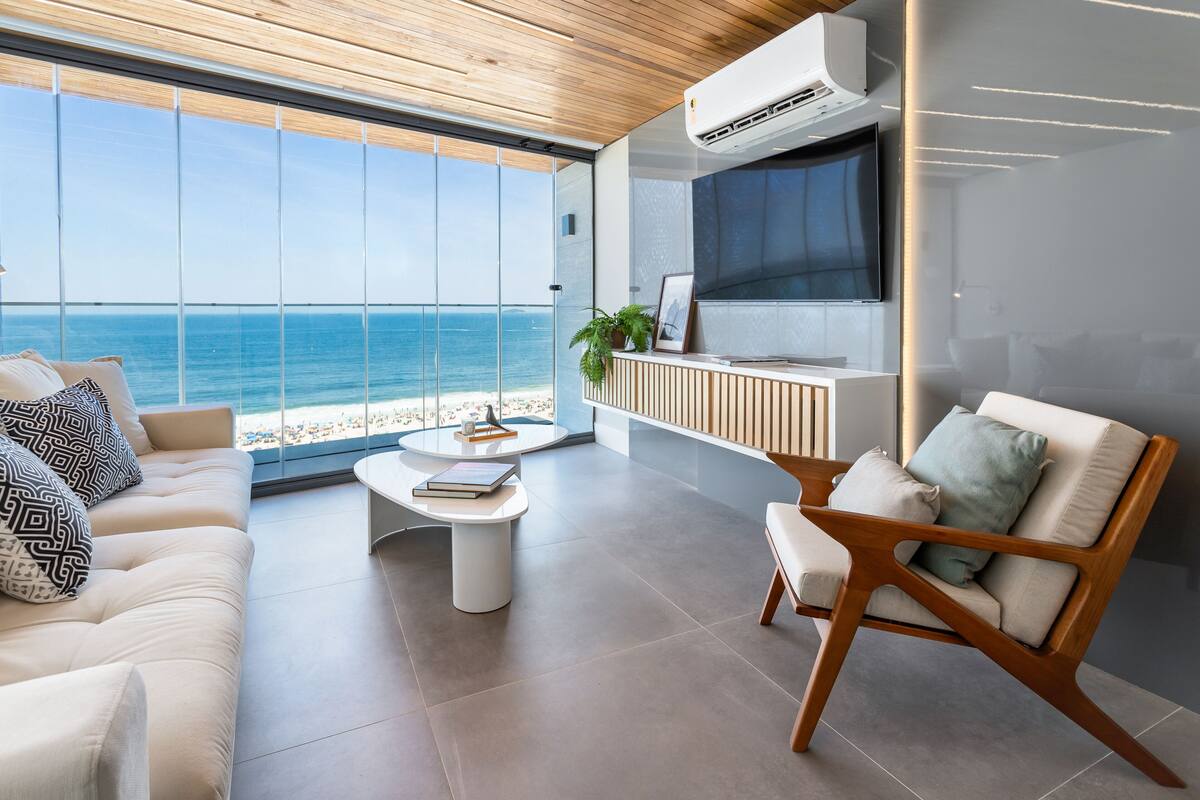 Ein modernes Wohnzimmer mit großem Fenster zum Strandblick, einer Couch, einem Couchtisch und einem Fernseher.
