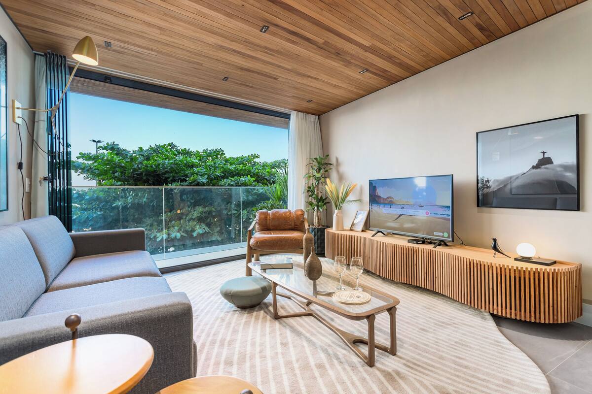 Ein modernes Wohnzimmer mit einer Couch, einem Couchtisch, einem Fernseher und einem Balkon mit Pflanzen.
