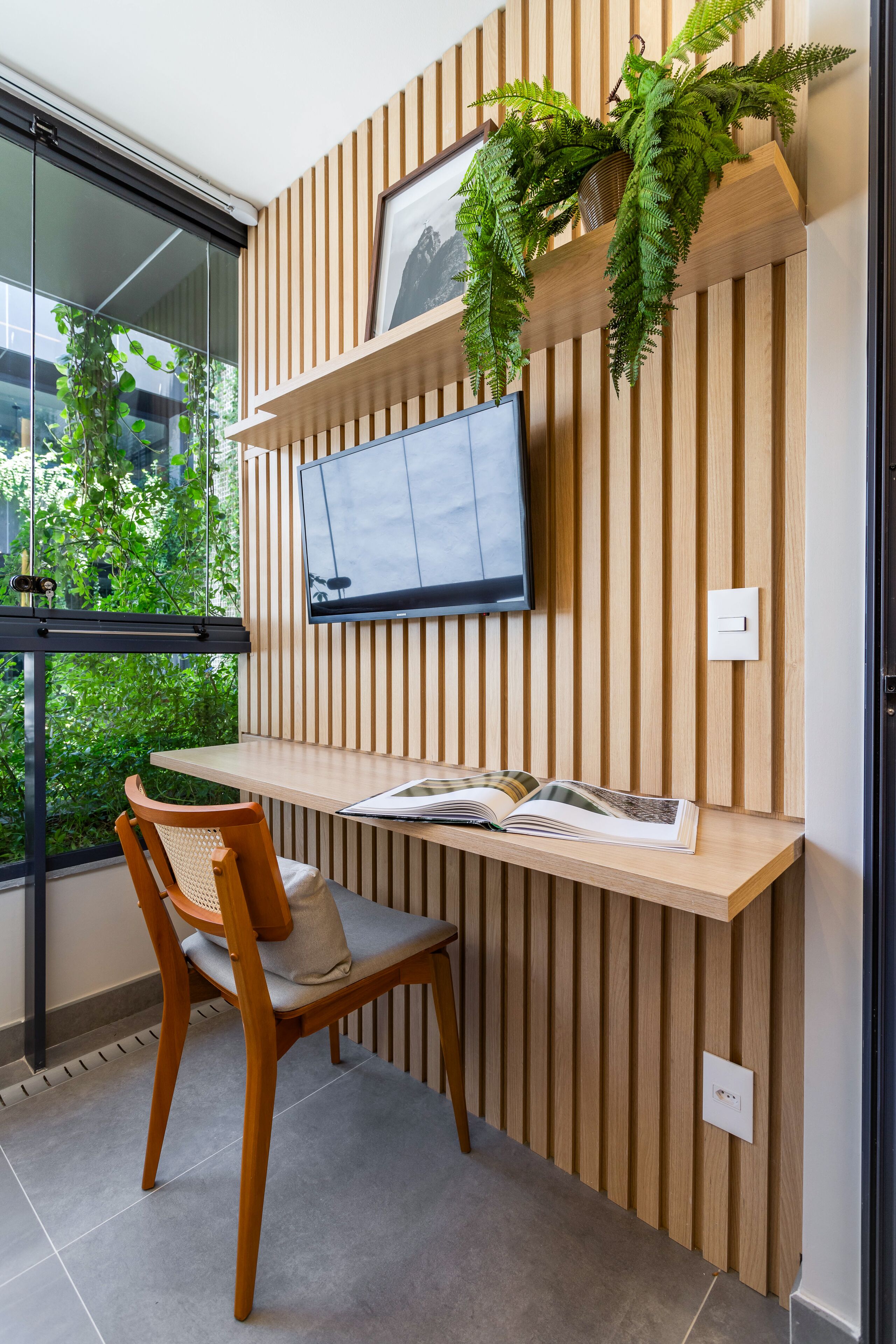 Un espacio de trabajo moderno con un panel de listones de madera, un televisor montado y un escritorio con una silla.