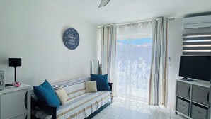 A living room with a sofa, TV, ceiling fan, and a clock on the wall. - V0742 - Apt 4 pers Vias Plage parking piscine collective (Vias)