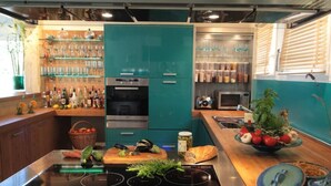 A modern kitchen with teal cabinets, a black induction cooktop, and a variety of kitchen appliances.