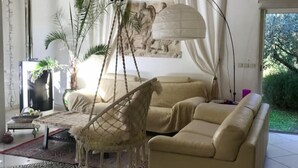 A cozy living room with a beige sofa, a hanging chair, and a large window with curtains.