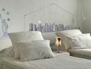 A hotel room with a bed, two pillows, a nightstand with a lamp, and a wall mural of a city skyline. - Villa de Reve Avec Jardin, Piscine et Option Spa (Uzès)