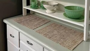 Une cuisine avec des meubles blancs, de la verrerie verte et un réfrigérateur blanc.