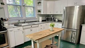 Une cuisine avec des meubles blancs, un réfrigérateur en acier inoxydable, un four à micro-ondes et une table en bois avec des tabourets.