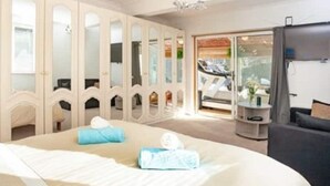 Un dormitorio con una cama grande, un armario con puertas espejadas, una mesita y una silla.