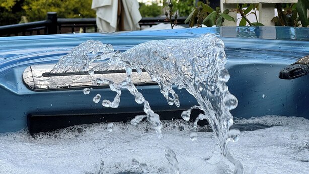 Un jacuzzi con agua salpicando, una sombrilla blanca y vistas al mar.
