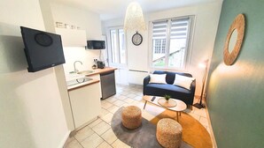 Un espacio habitable compacto con kitchenette, un sofá, una mesa de centro y un televisor en la pared.