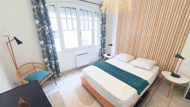 Un dormitorio con cama, una silla, un escritorio, una lámpara y una ventana con cortinas.