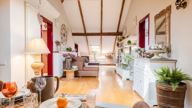 A cozy living room with a wooden ceiling, a dining area with a table set for two, and a kitchen in the background. - The Rooftop Penthouse (Lucca)