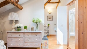A room with a wooden ceiling, a white dresser with heart-shaped handles, a lamp, and a vase with flowers. - The Rooftop Penthouse (Lucca)