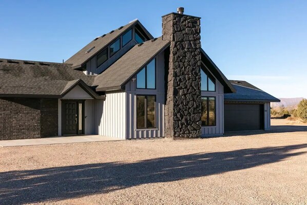 Una casa moderna de dos pisos con chimenea de piedra, ventanas amplias y garaje.