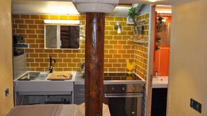 A compact kitchen with a brick backsplash, a central island, and a wooden column. - Maisonnette Avec Terrasse Dentrée et Balcon (Uzès)