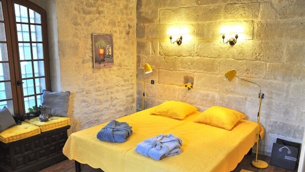A room with a bed, two bedside lamps, a window, a bench, and a wall-mounted picture. - Maisonnette Avec Terrasse Dentrée et Balcon (Uzès)